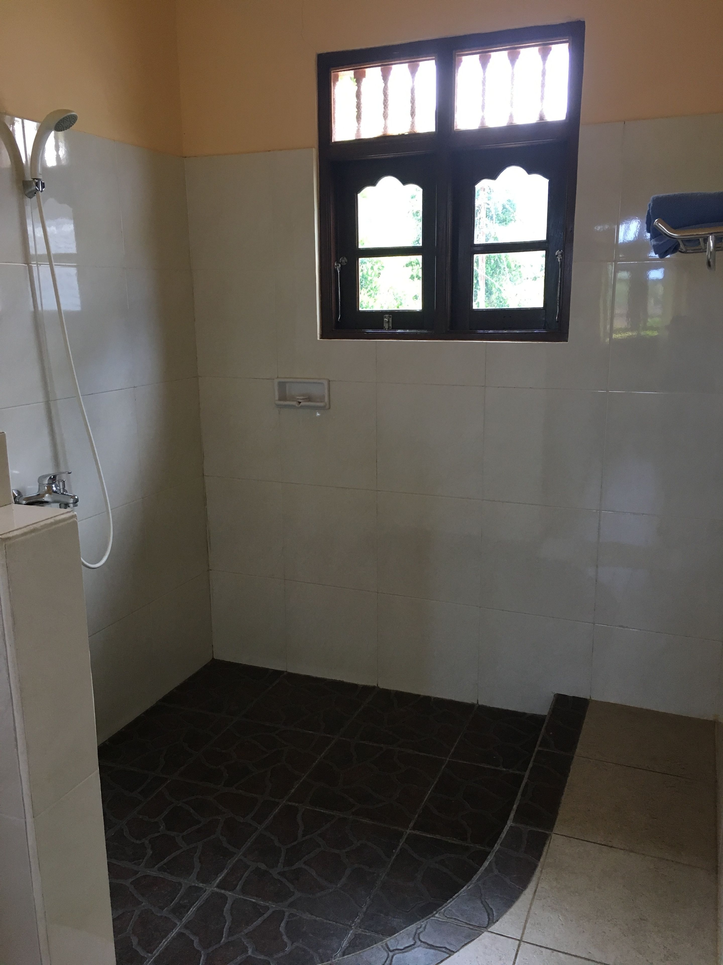 A bathroom with a shower, a window, and a tiled floor.