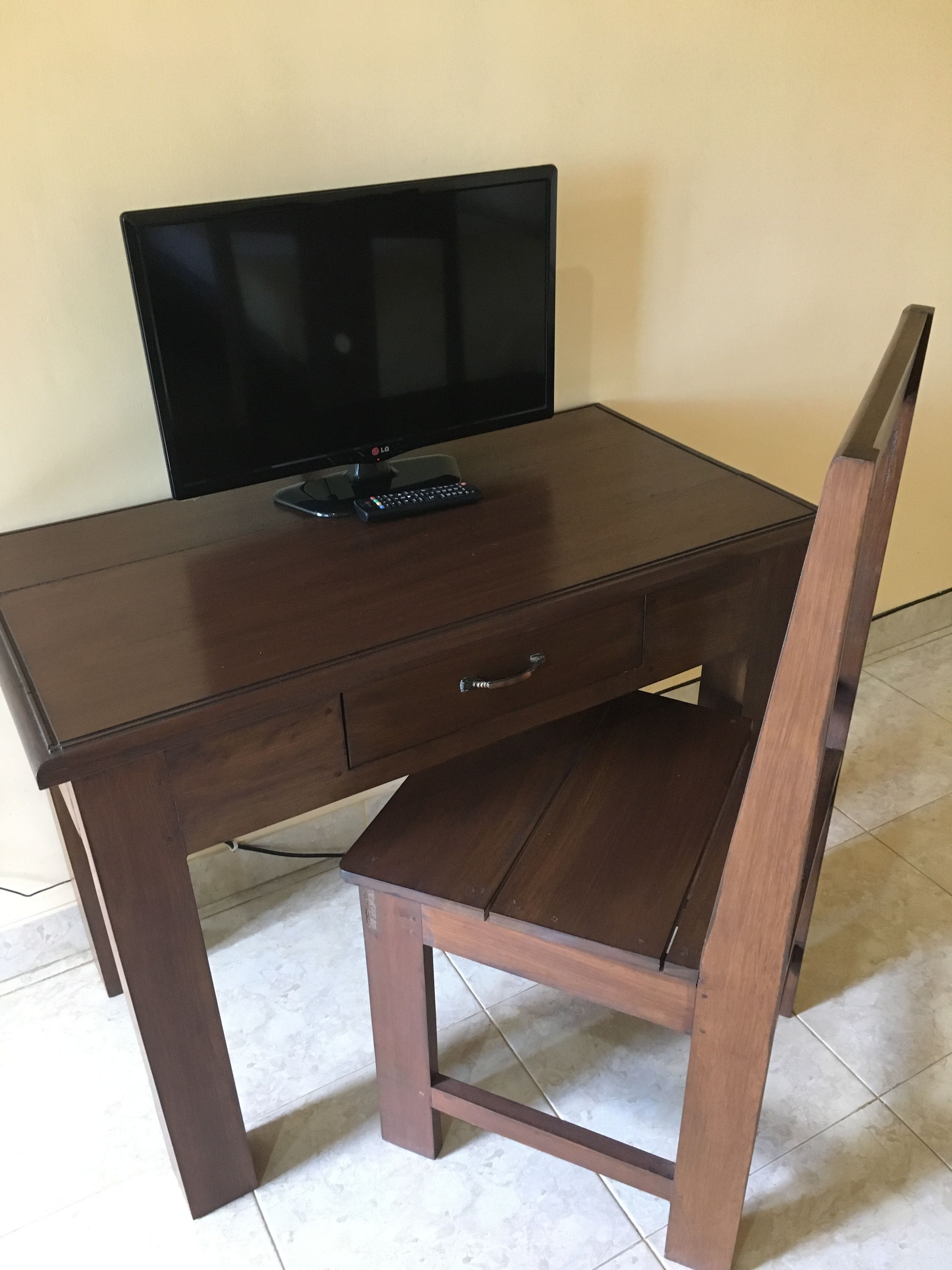 A wooden desk with a television, a drawer, and a chair.