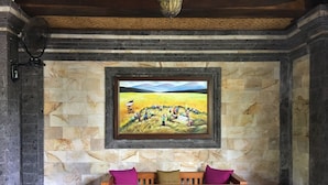 Un coin repas agrémenté d’un mur en pierre, d’un tableau représentant un paysage rural et d’une table en bois avec des chaises.
