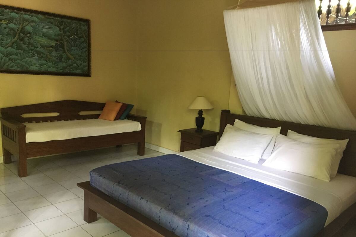 A bedroom with a bed, a bench, a nightstand, a lamp, and a painting on the wall.