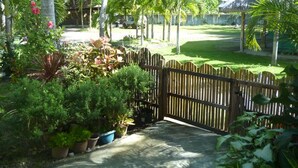A tropical garden with a wooden fence, palm trees, and potted plants. - Alma's Guesthouse (Panglao)