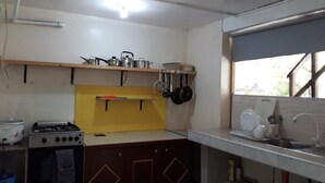 A compact kitchen with a gas stove, a sink, and a yellow backsplash. - Alma's Guesthouse (Panglao)