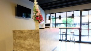 A reception desk with a large window, a flat-screen TV, and a vase with flowers. - Livinn Hostel City Center Surabaya (Surabaya)