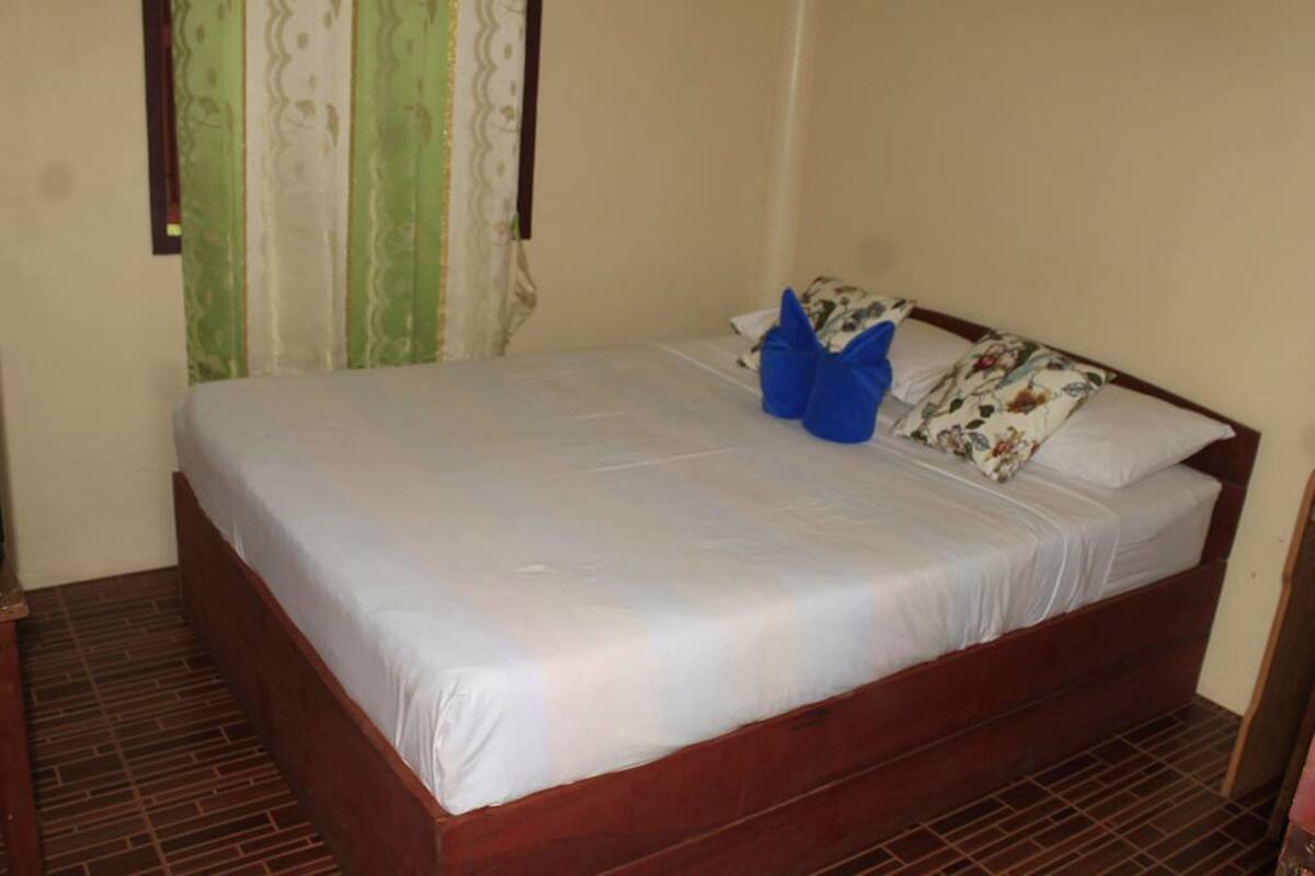 Una cama individual con estructura de madera, ropa de cama blanca y dos almohadas azules.