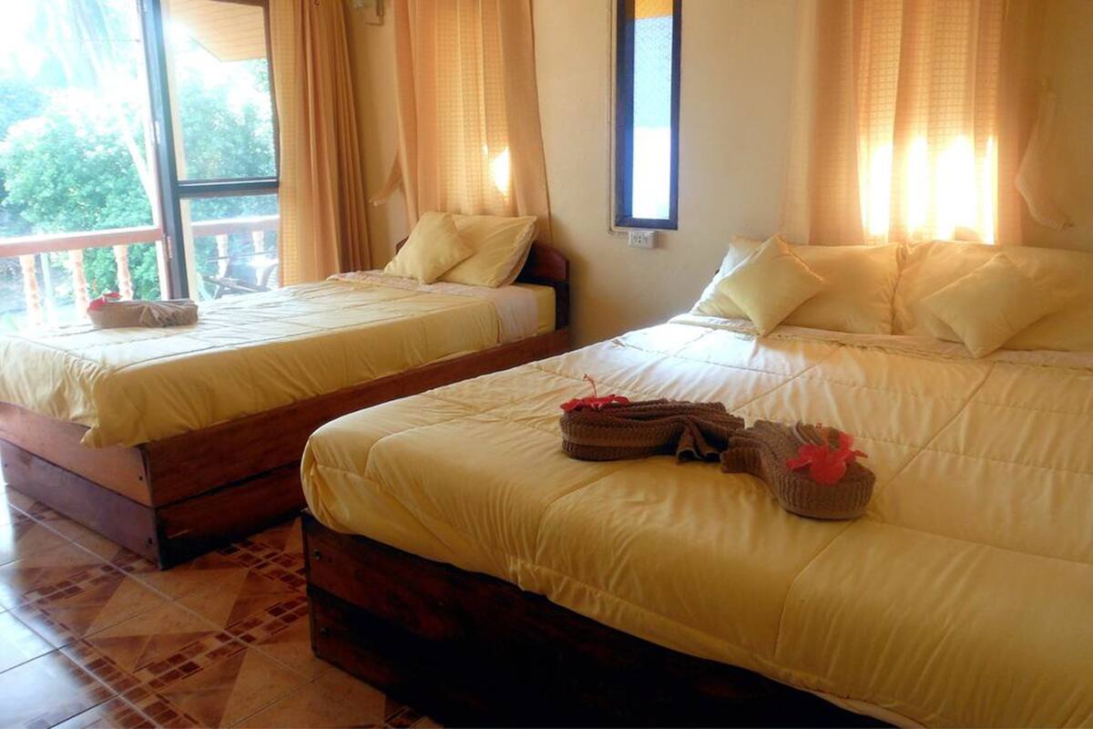 Dos camas dobles con ropa de cama a juego, piso de madera y una ventana con cortinas.
