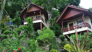 Un edificio de dos pisos con un balcón, rodeado de abundante vegetación y plantas tropicales.