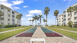 Un patio con dos canchas de rifa, un banco blanco y palmeras.