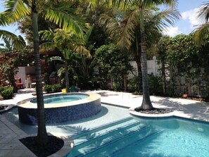 A swimming pool with a tiled edge, surrounded by palm trees and a white fence.