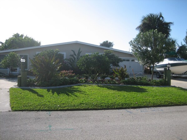 A residential house with a well-maintained lawn, a small garden with various plants, and a boat parked in the driveway.