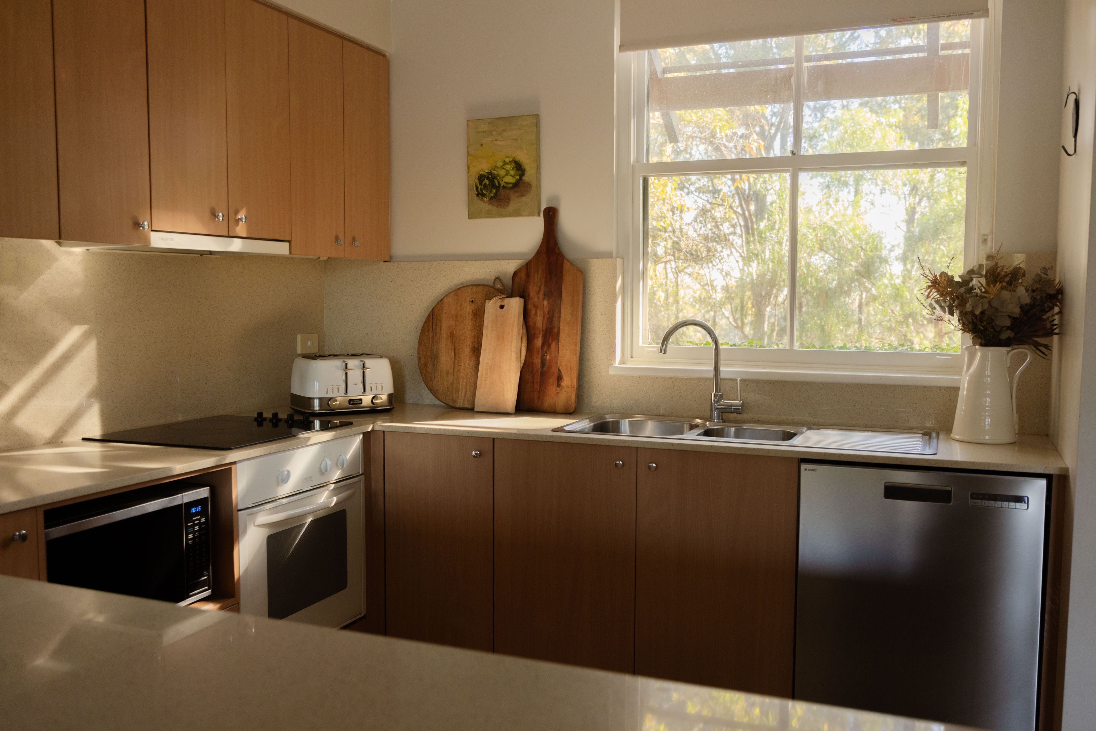 Une cuisine moderne avec des meubles en bois, un lave-vaisselle en acier inoxydable et une fenêtre donnant sur les arbres.