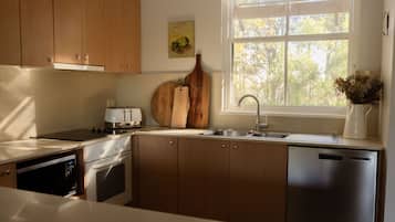 Une cuisine moderne avec des meubles en bois, un lave-vaisselle en acier inoxydable et une fenêtre donnant sur les arbres.