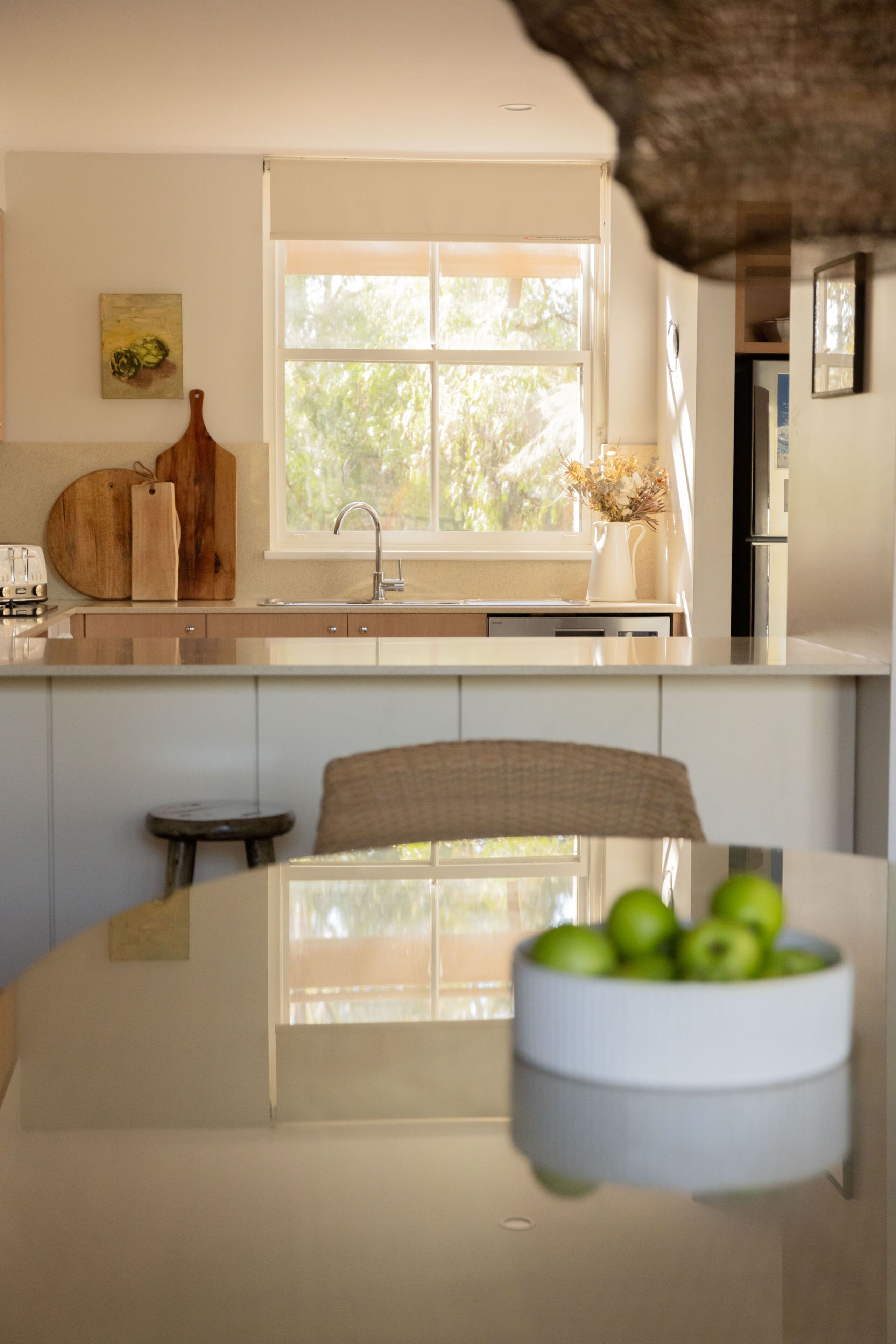 A modern kitchen with a large window, a dining table with a bowl of fruit, and a rustic chair.