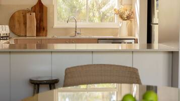 A modern kitchen with a large window, a dining table with a bowl of fruit, and a rustic chair.