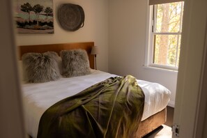A bed with a wooden headboard, two fluffy pillows, a green blanket, and a painting on the wall.