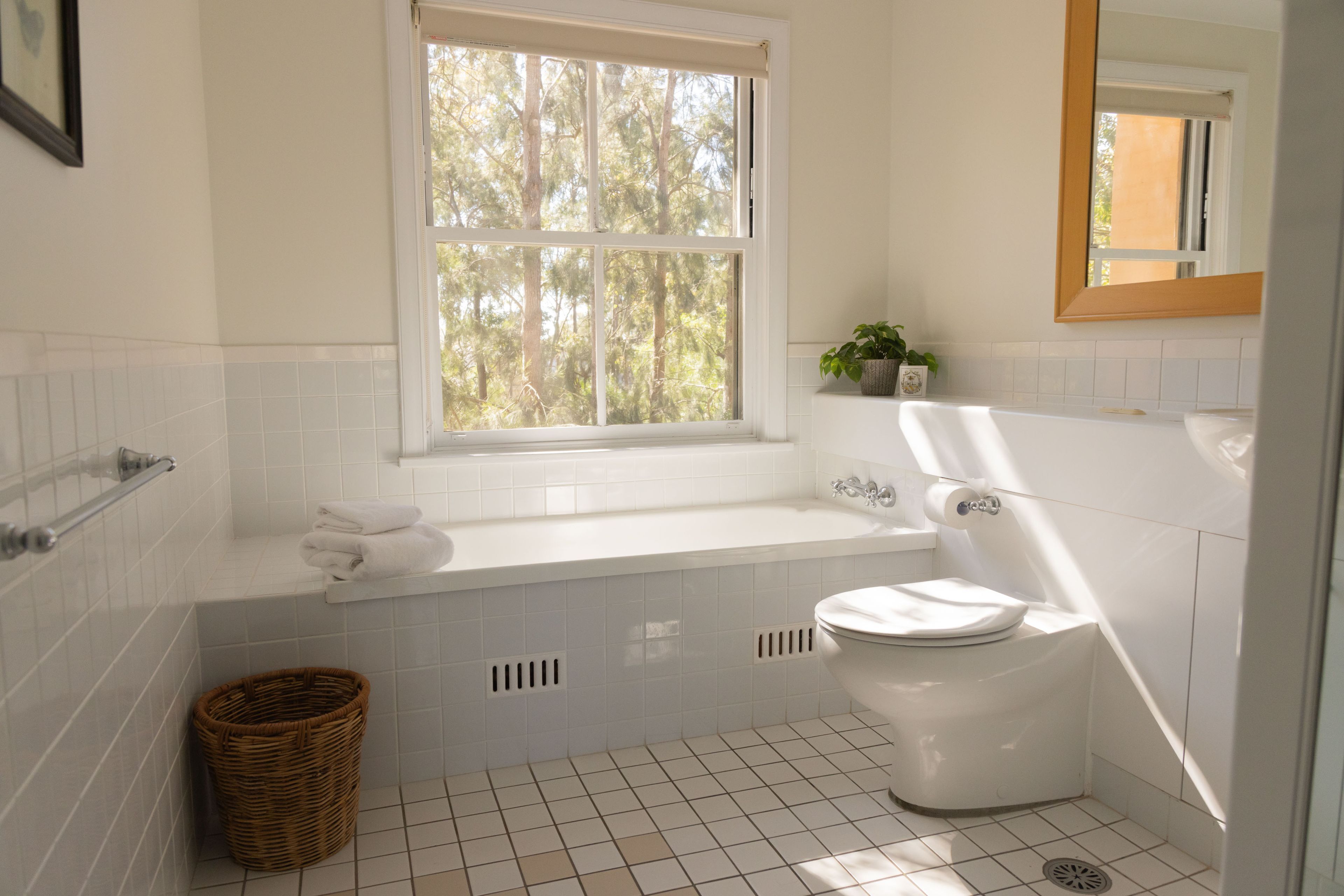 A bathroom with a white bathtub, toilet, and a window with a view of trees.