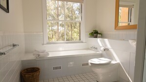 A bathroom with a white bathtub, toilet, and a window with a view of trees.