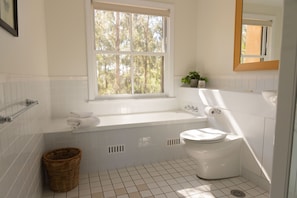 Un baño con una bañera blanca, inodoro y ventana con vista a árboles.