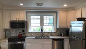 Une cuisine moderne avec des armoires blanches, des appareils en acier inoxydable, une fenêtre offrant une belle vue et un dosseret carrelé.