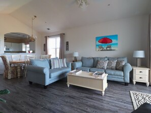 A living room with a sofa, coffee table, and a painting of a beach scene.