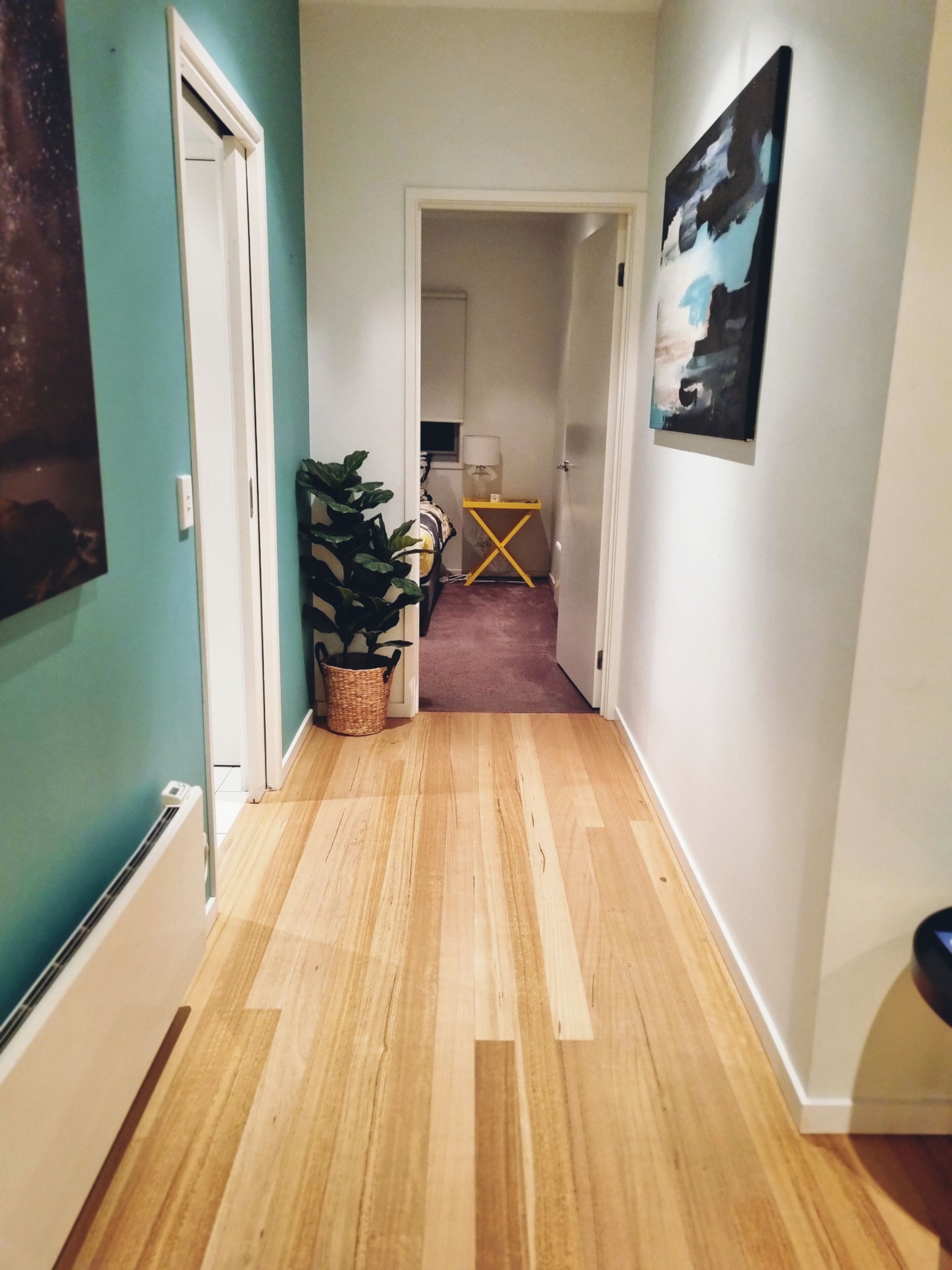 A narrow hallway with wooden flooring, a potted plant, and a yellow table.