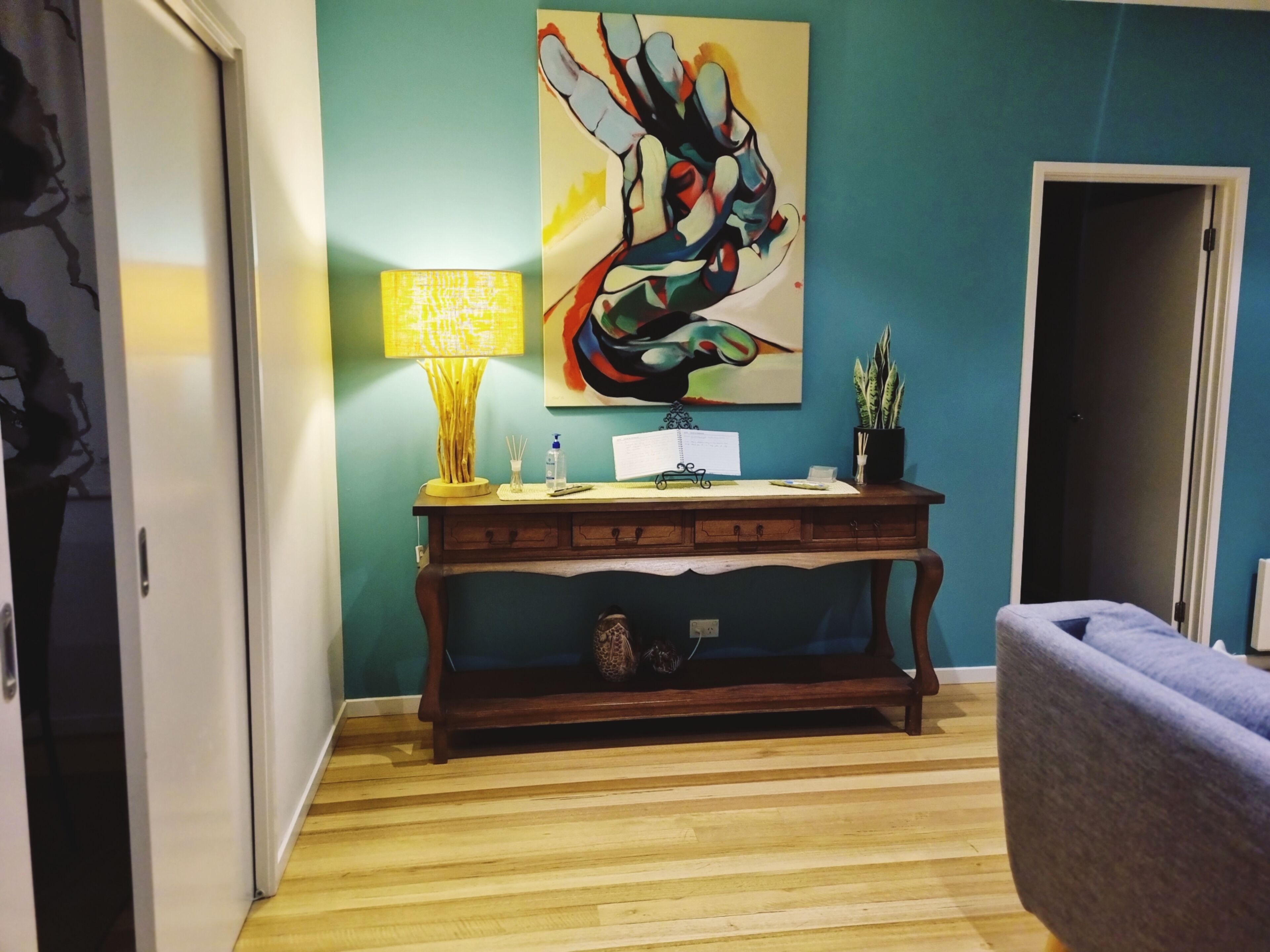 Um quarto com uma mesa de consola de madeira, uma luminária, um quadro e uma cadeira.