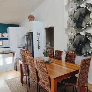 Ein stilvoller Essbereich mit Holztisch und gewebten Stühlen, im Hintergrund eine Küche und ein großes abstraktes Gemälde an der Wand.