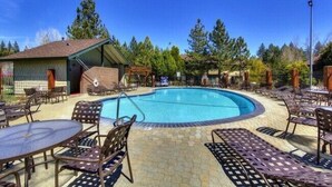 A pool area with lounge chairs and tables, surrounded by trees.