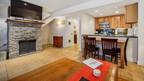 A modern kitchen with wooden cabinets, a stone fireplace, and a dining area with a red rug and a book on the table.