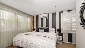 A bedroom with a bed, bedside tables, an air conditioning unit, and a window with curtains. - The Hidden Door Bowral Villa - the Heart of Bowral (Bowral)
