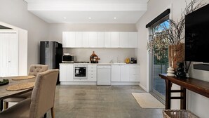 A modern kitchen with white cabinets, a black refrigerator, and a dining area with a wooden table and chairs. - The Hidden Door Bowral Villa - the Heart of Bowral (Bowral)