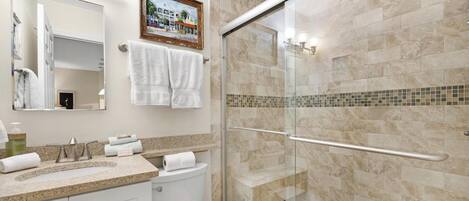 Un baño moderno con ducha de vidrio, lavabo con encimera de mármol y retrete.