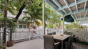 A covered outdoor patio with wicker furniture, a white picket fence, and lush greenery. - Another Three Hour Tour at The Truman Annex in Key West (Key West)