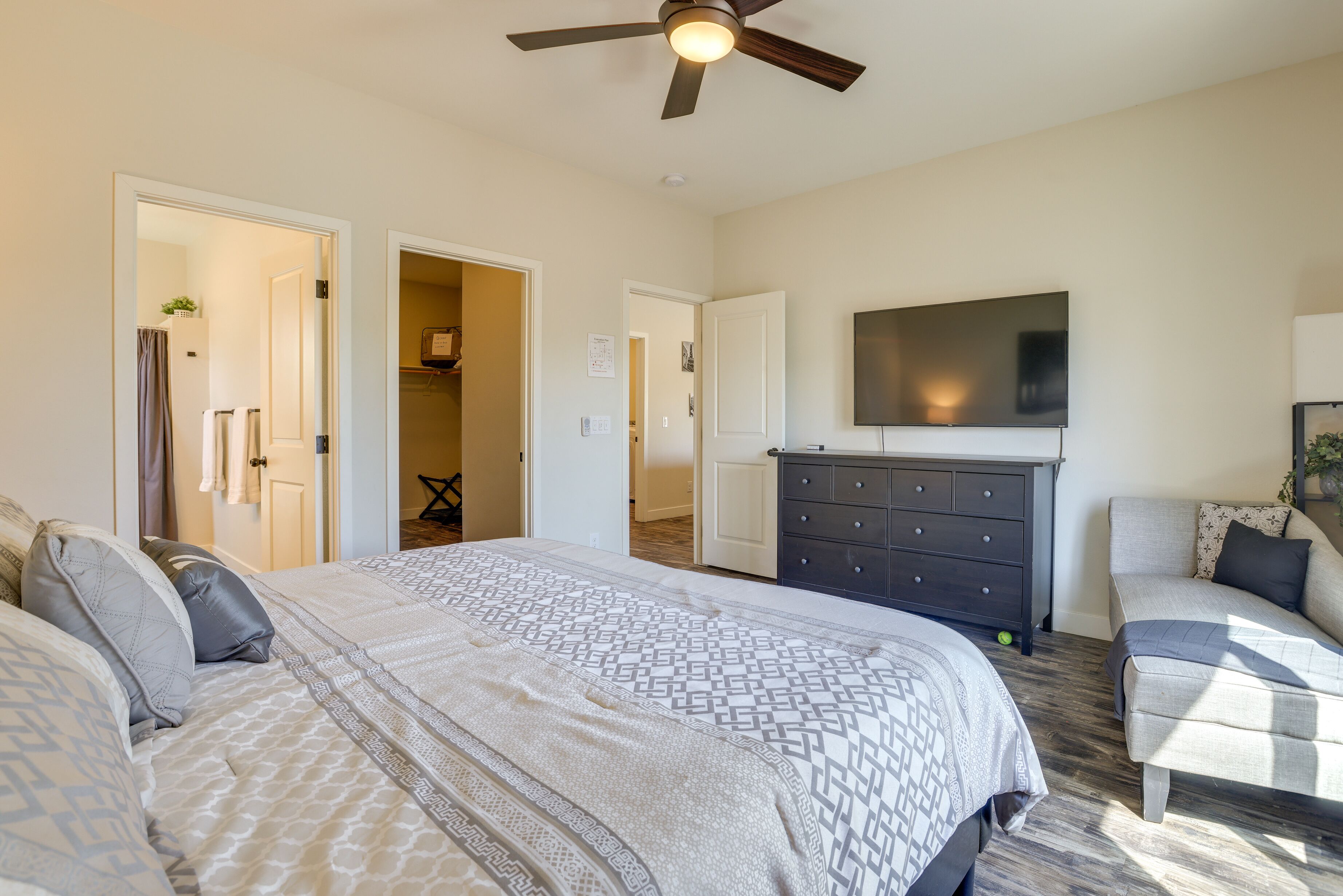 A bedroom with a large bed, a dresser, a TV on the wall, and a ceiling fan.