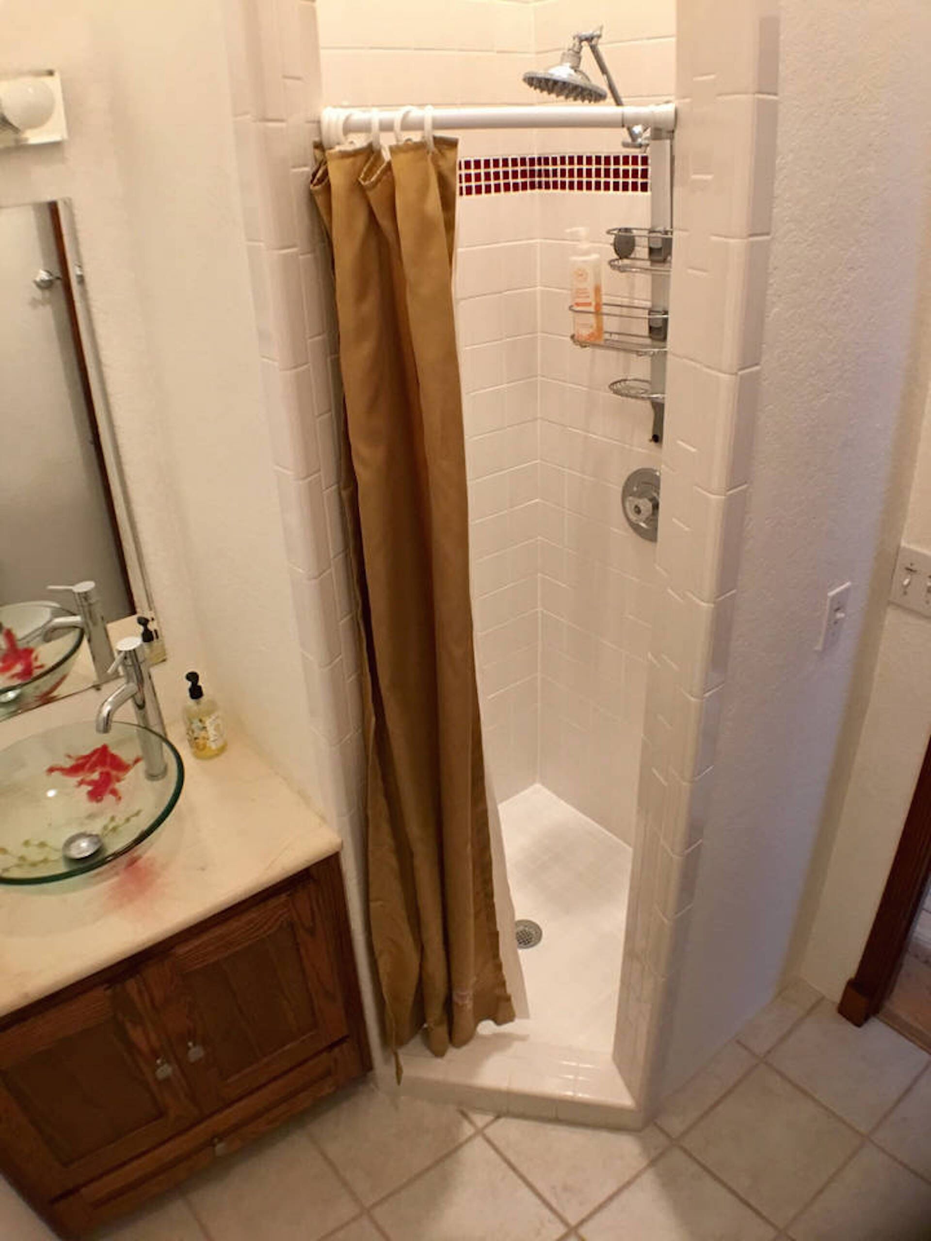 A bathroom with a glass sink, a wooden cabinet, a shower with a beige curtain, and a tiled floor.