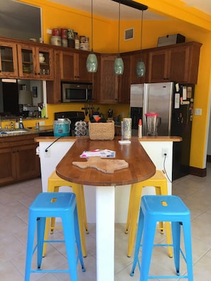A kitchen with wooden cabinets, a central island with stools, and a refrigerator.