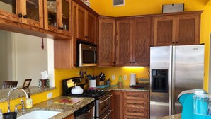 A kitchen with wooden cabinets, stainless steel appliances, granite countertops, and a yellow wall.