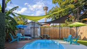 A backyard with a swimming pool, lounge chairs, a wooden deck, and a view of a tower.