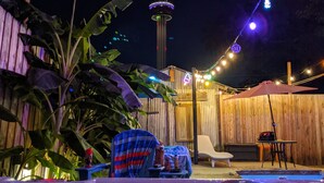 A backyard with a swimming pool, a wooden fence, and a view of a tower with lights.