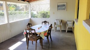 Un patio techado con una mesa redonda y cuatro sillas, un taburete pequeño y una pared amarilla con una placa.