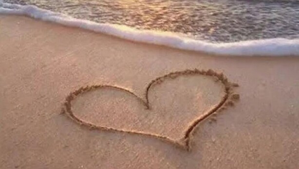Una playa con un dibujo de arena en forma de corazón y un atardecer sobre el océano.