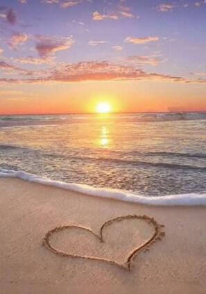 Una playa con un dibujo de arena en forma de corazón y un atardecer sobre el océano.