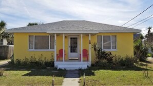 Una casa amarilla con porche, dos ventanas y una puerta.