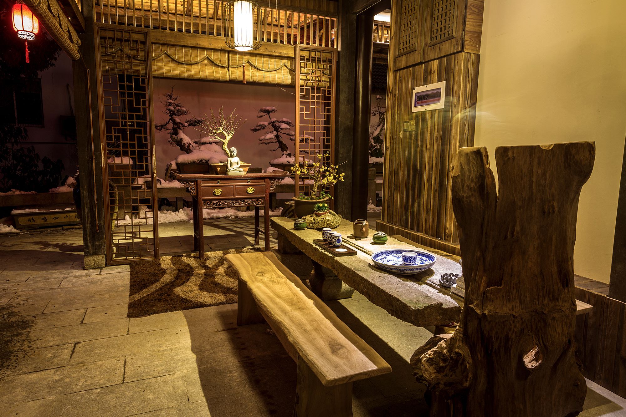 Interior de madera tradicional con un banco de piedra, una mesa con juego de té y un bonsái.