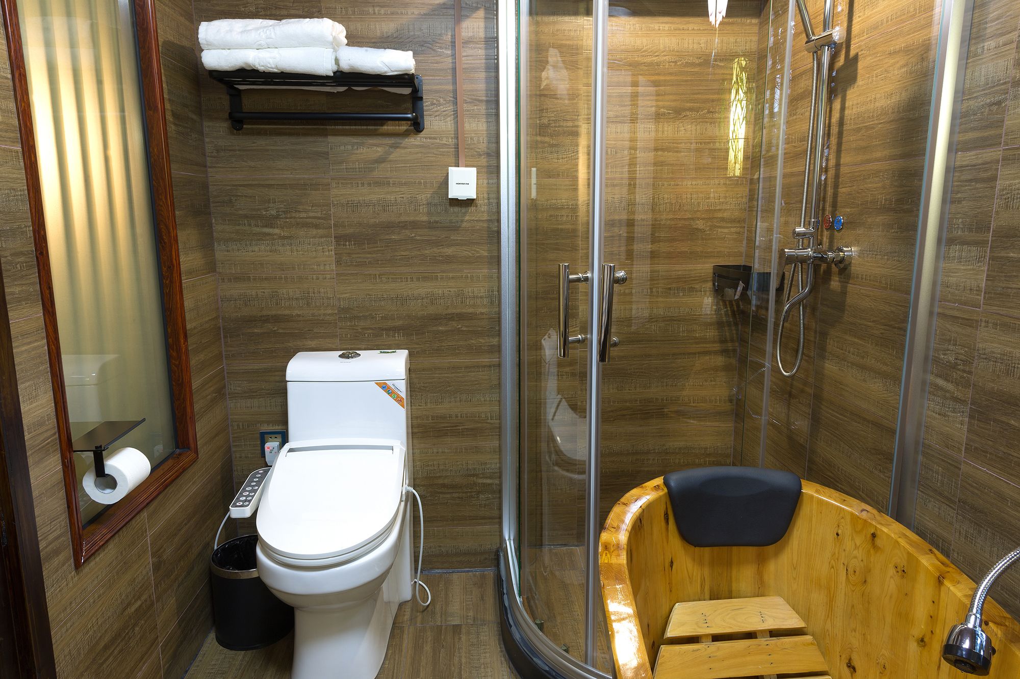 Et moderne badeværelse med toilet, bruser og et trævandsbadekar.