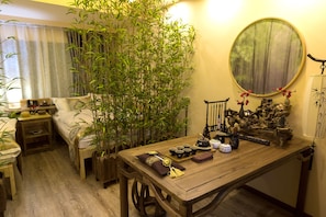 A traditional Japanese-style room with a wooden table, a sofa, and a large bamboo plant. - FTYS Hostel (Hangzhou)