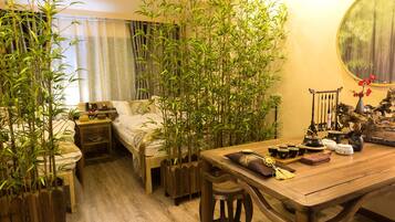 A traditional Japanese-style room with a bed, a wooden table with tea set, and bamboo plants.