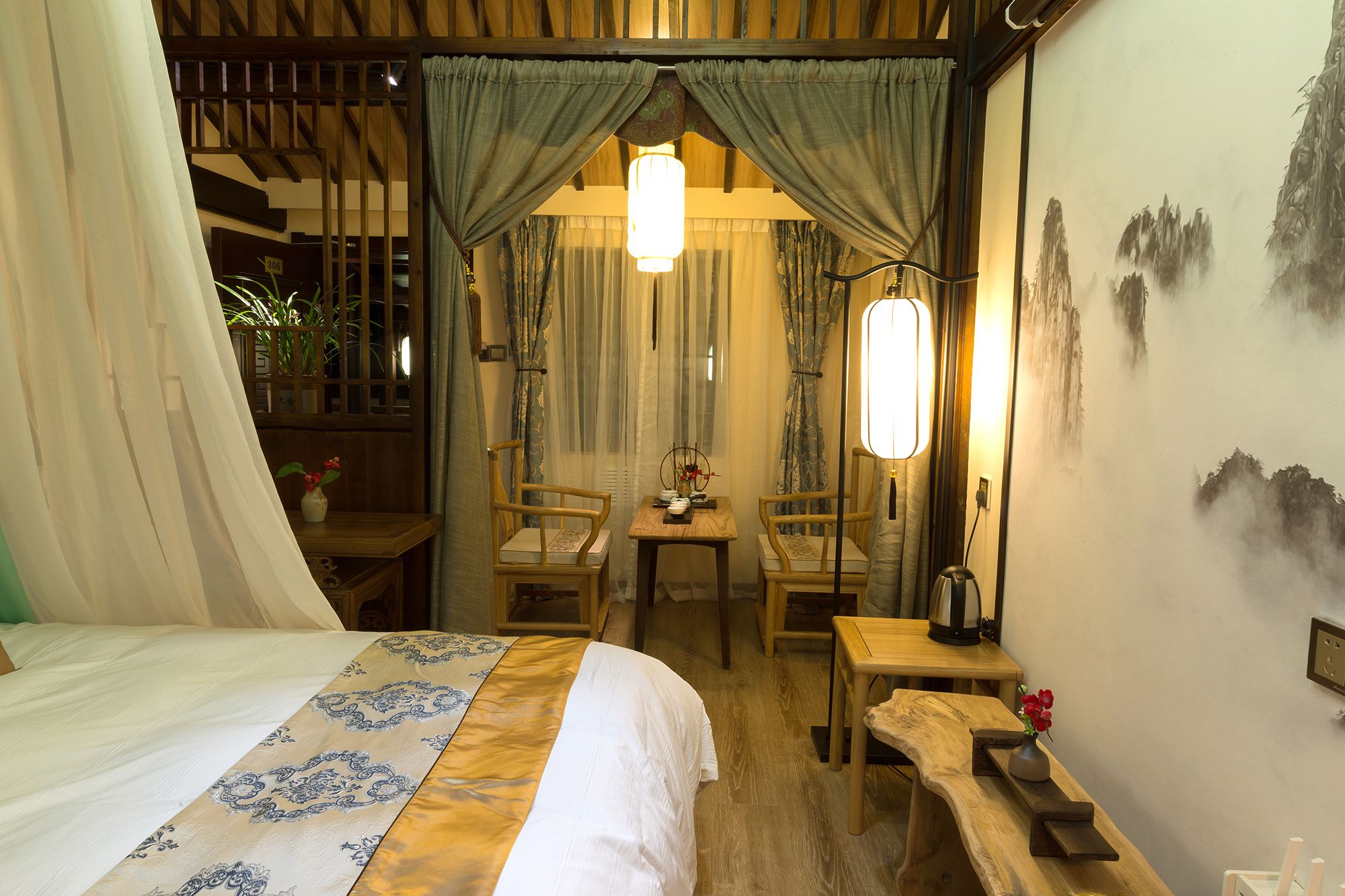 A traditional room with a bed, two chairs, a table, and a wall painting.