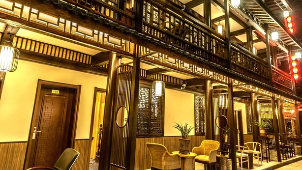 Un bâtiment traditionnel doté d’un balcon en bois, de plusieurs portes et d’un espace détente avec des chaises et des tables.