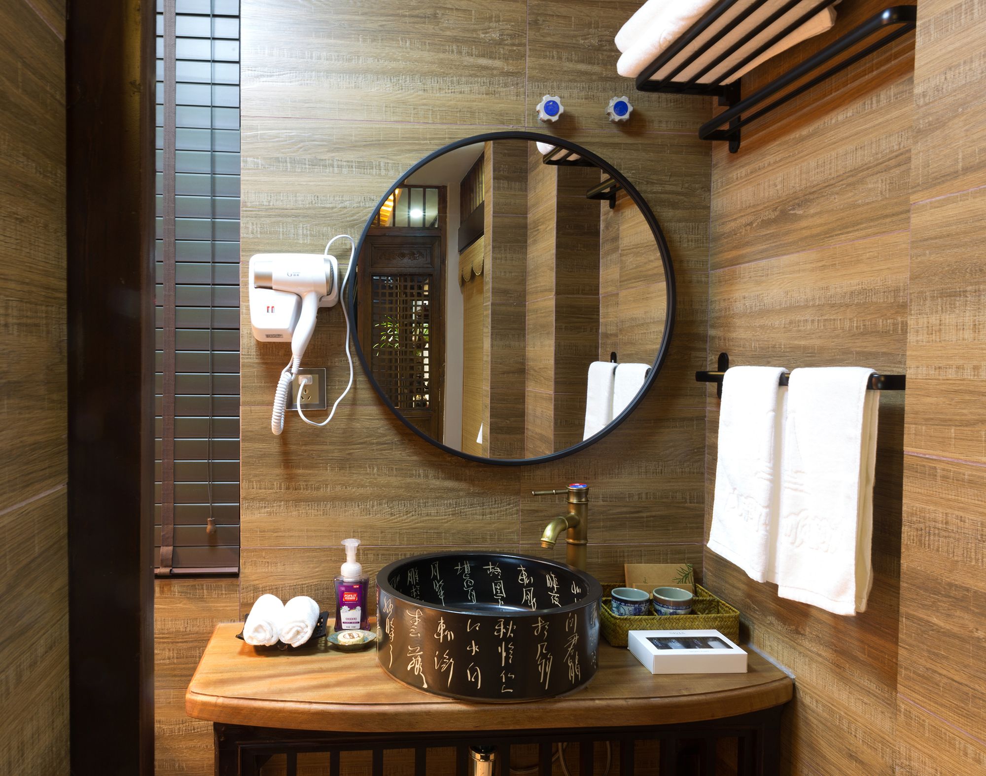 Un baño con tocador de madera, un espejo redondo, un secador de pelo, un lavabo y toallas.