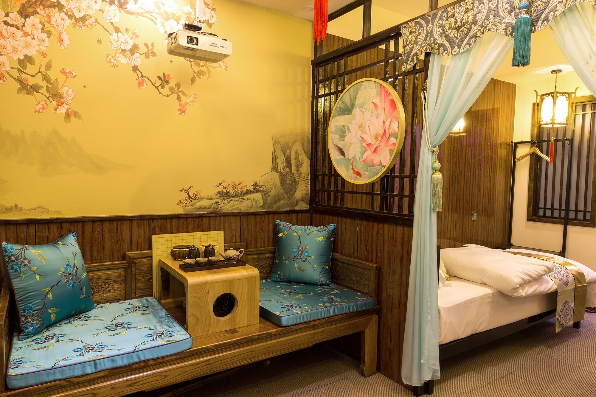 Une chambre au décor traditionnel, avec un lit en bois, un banc rembourré agrémenté de coussins à motifs floraux, un projecteur mural et un paravent décoratif.